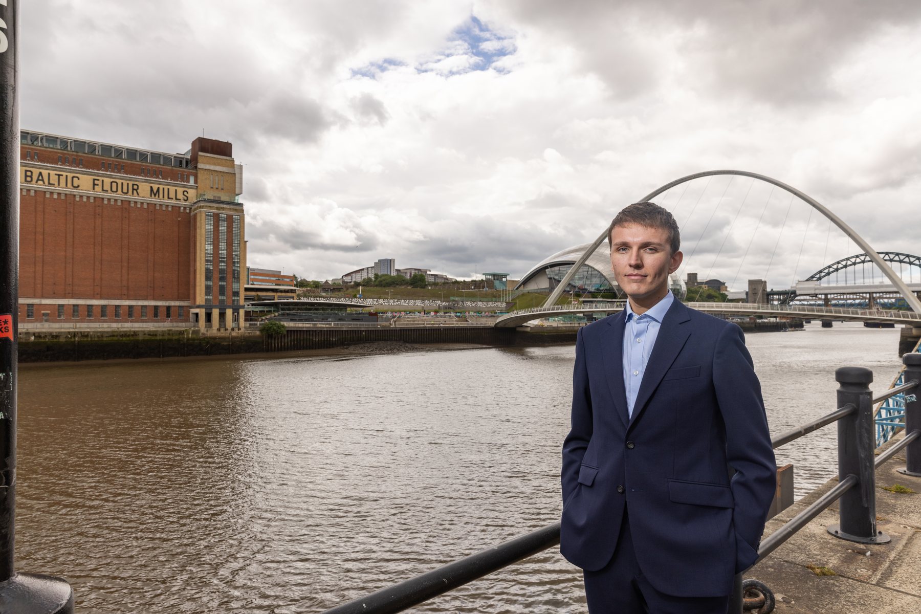Sebastian Moore beside the River Tyne with the Sage Gateshead and Millennium Bridge behind him